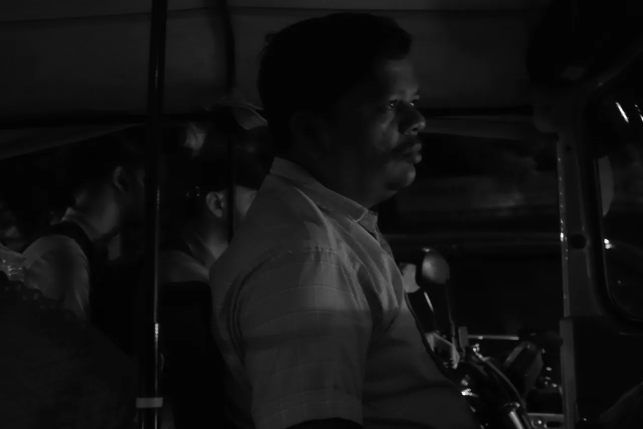 A man standing beside a vehicle at night, in black and white