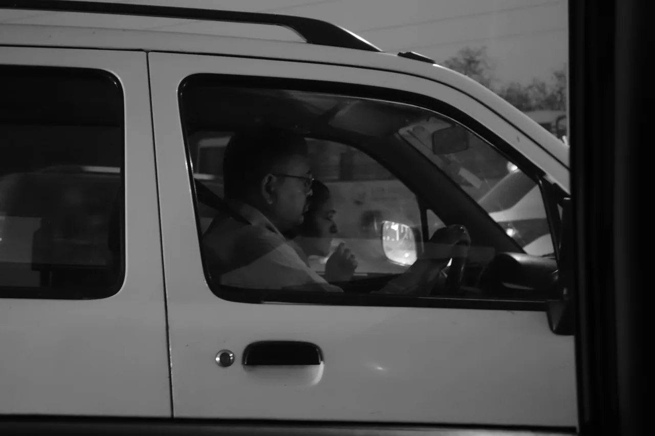 A driver seen through the side window of a white vehicle