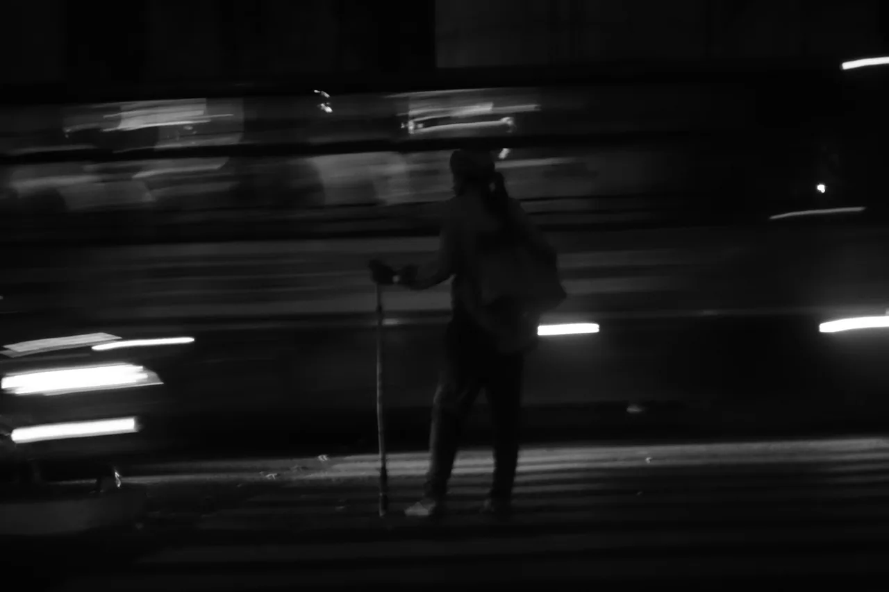A person silhouetted against blurred passing traffic