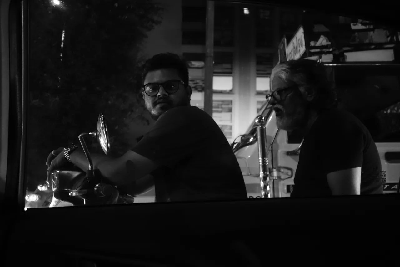 Two people beside a vehicle in the shadows of a city street