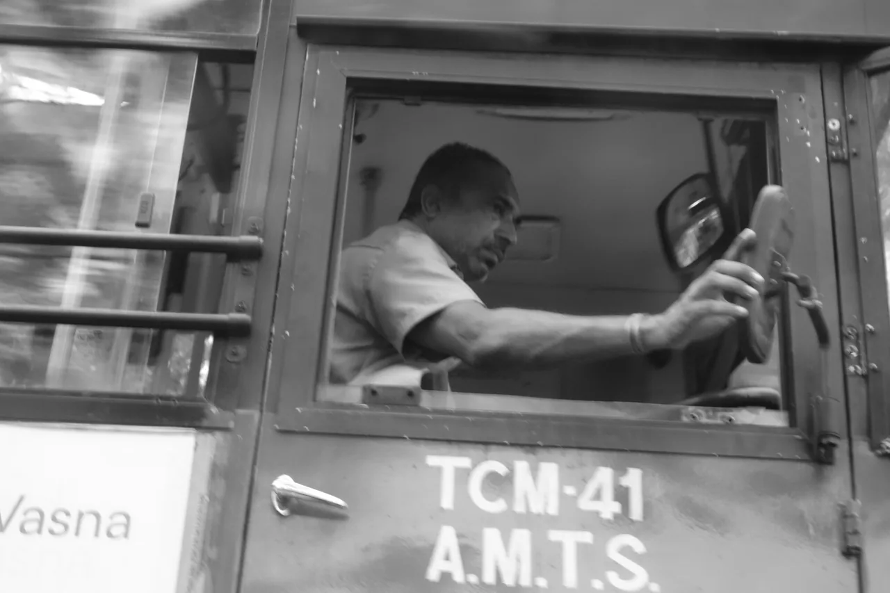 A bus driver at the wheel, viewed through the open side window