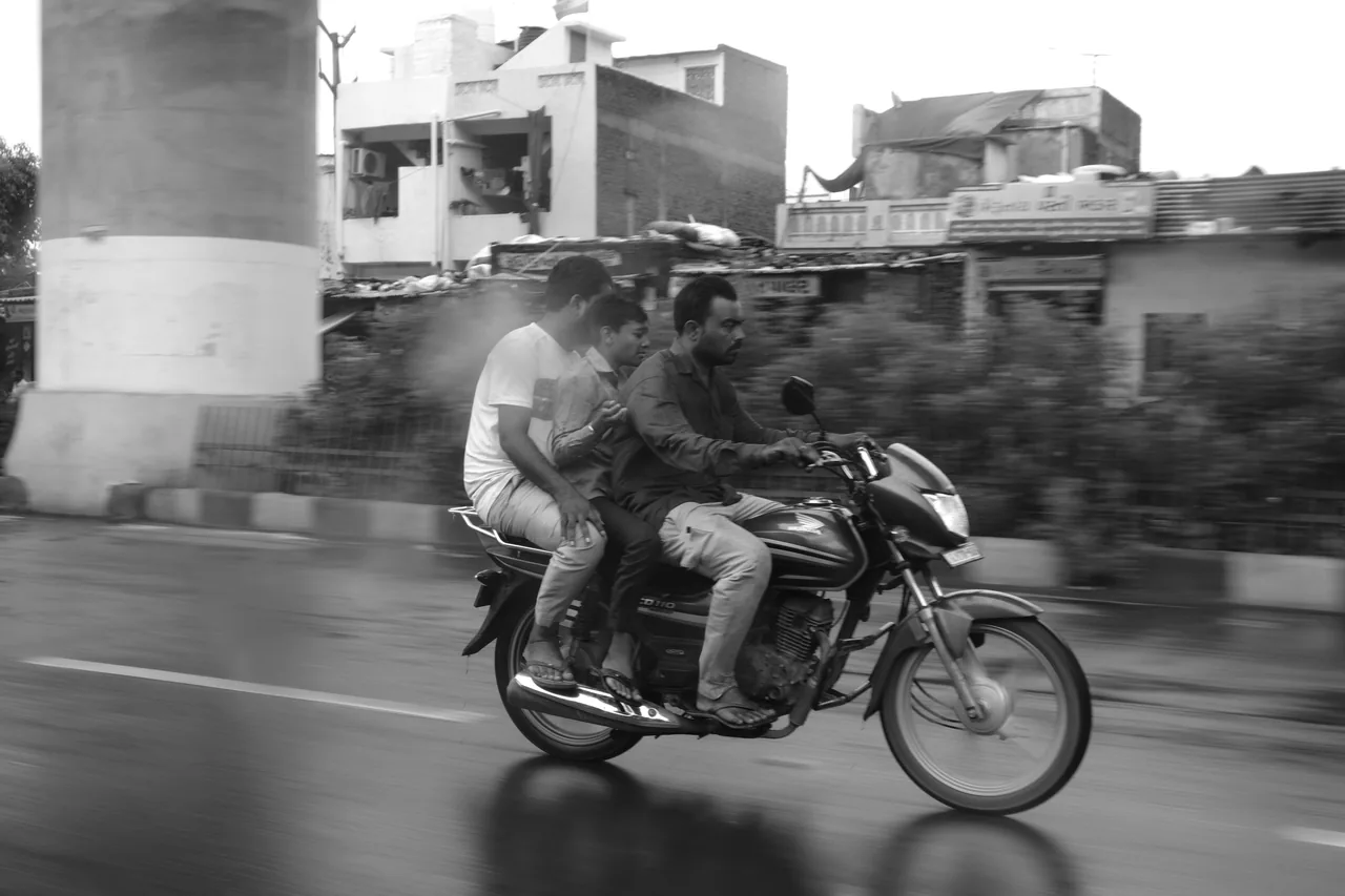 Two people riding a motorcycle past low buildings