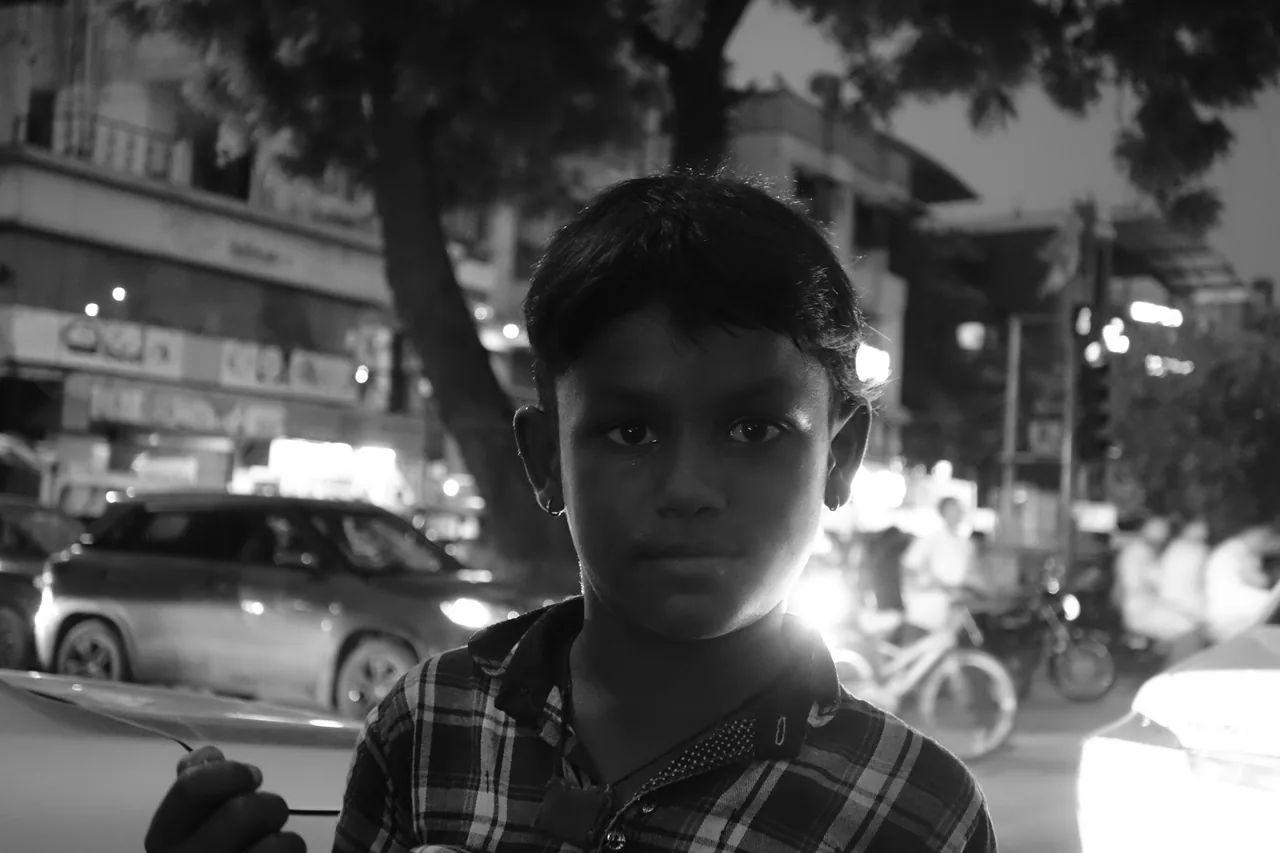 A boy looking towards the camera on a busy evening street