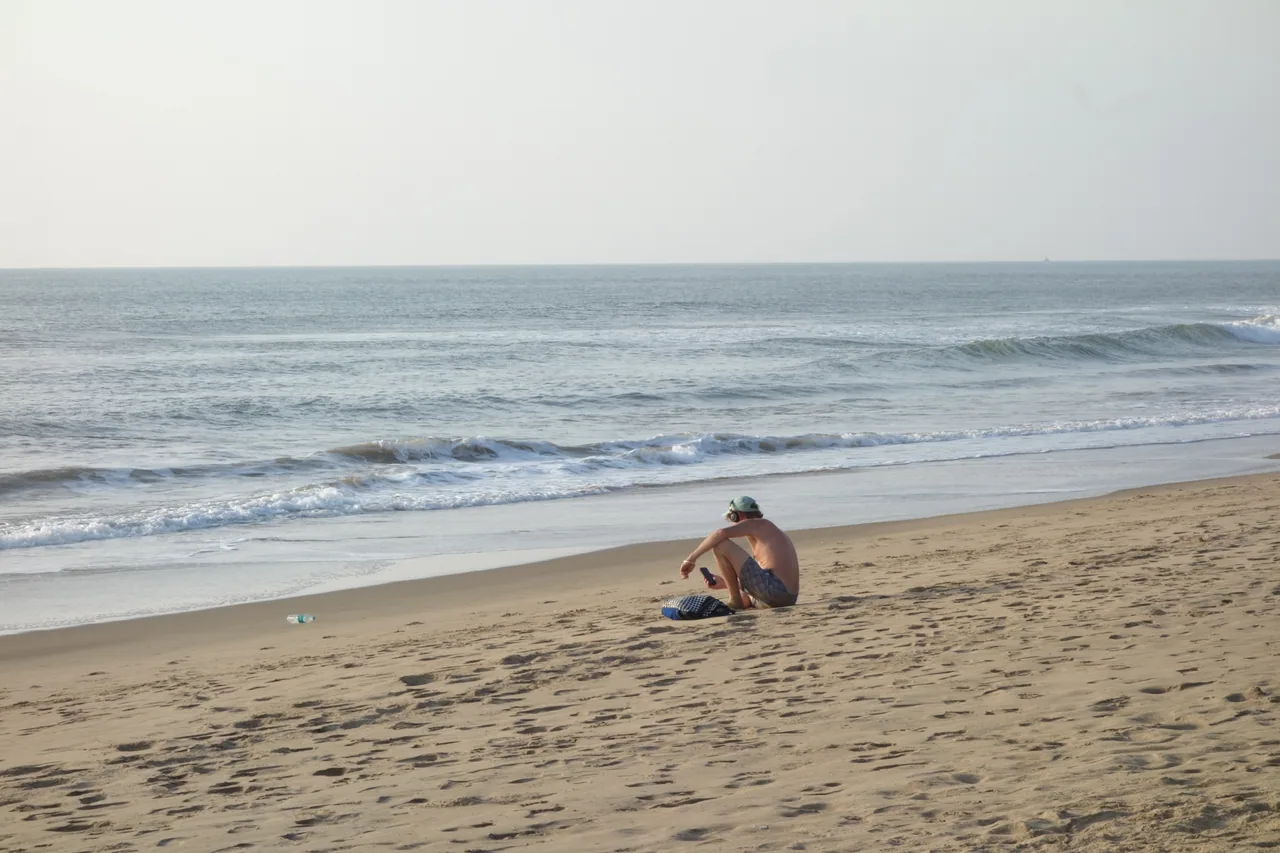 A person sitting on the beach facing the waves