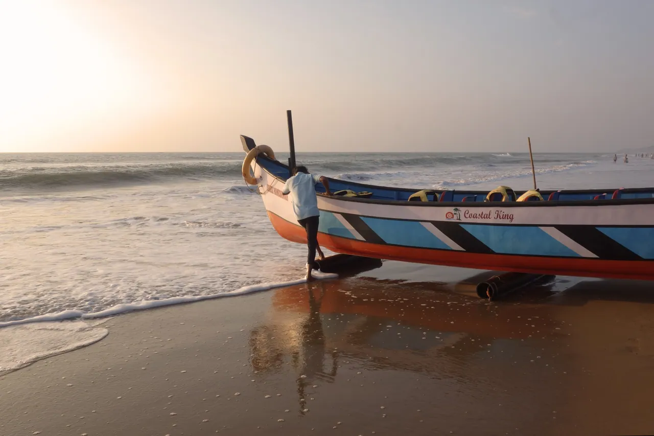A colourful fishing boat reflected in wet sand beside the sea