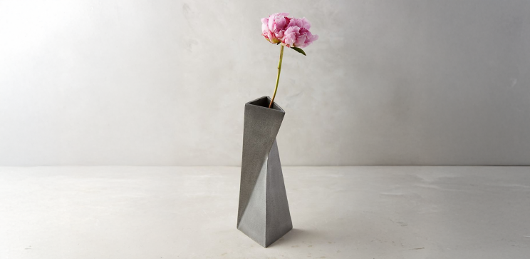 Reference photograph of a folded geometric cement vase with a pink flower